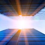 Tall modern skyscraper reflecting sunlight with a clear blue sky.