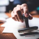 Hand stamping 'Approved' on a document at a desk.
