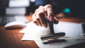 Hand stamping 'Approved' on a document at a desk.