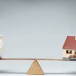 Piggy bank and house on a seesaw representing property investment balance.