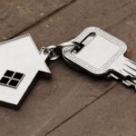 House key attached to a house-shaped keychain on wooden surface.