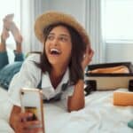 Smiling woman with a hat using her phone in a hotel room.