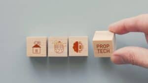 Hand placing PropTech wooden block among other property-themed blocks.
