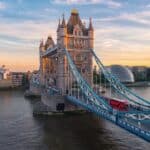 Iconic London Tower Bridge with a red double-decker bus crossing at sunset.