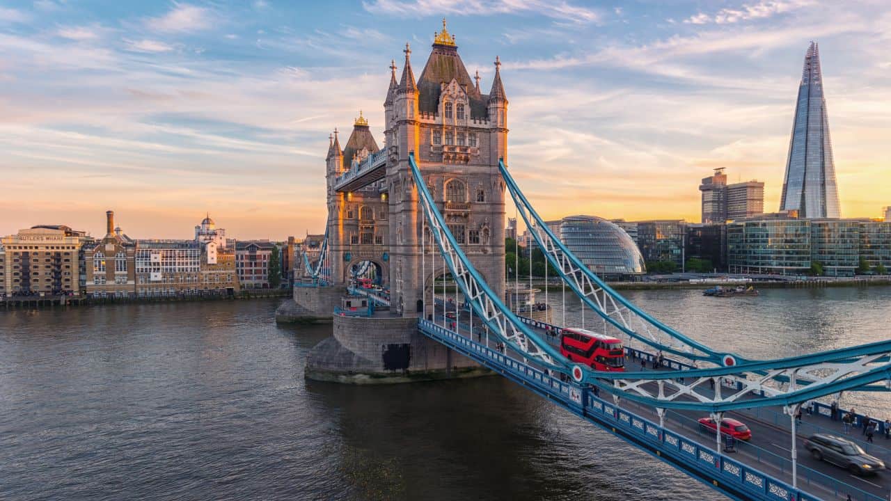 Iconic London Tower Bridge with a red double-decker bus crossing at sunset.