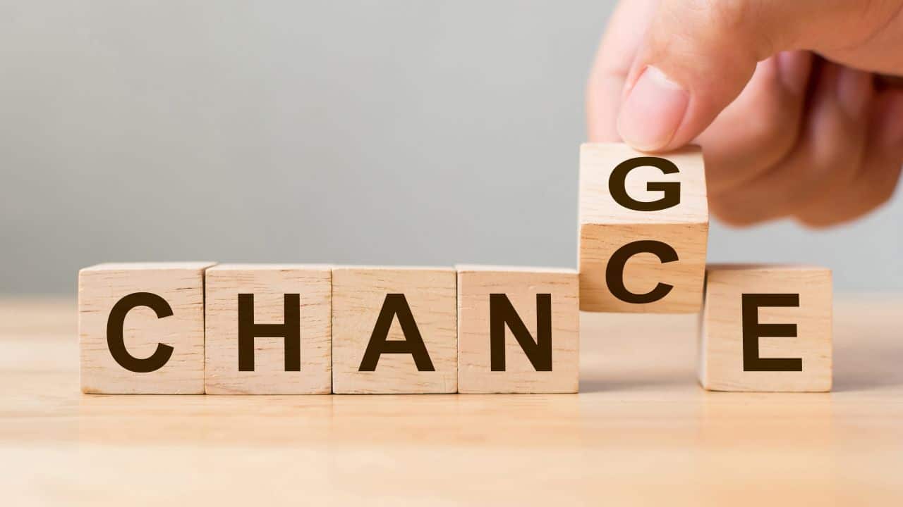 Hand placing a wooden block with 'G' on top of 'C' in a sequence of blocks spelling 'CHANGE'.